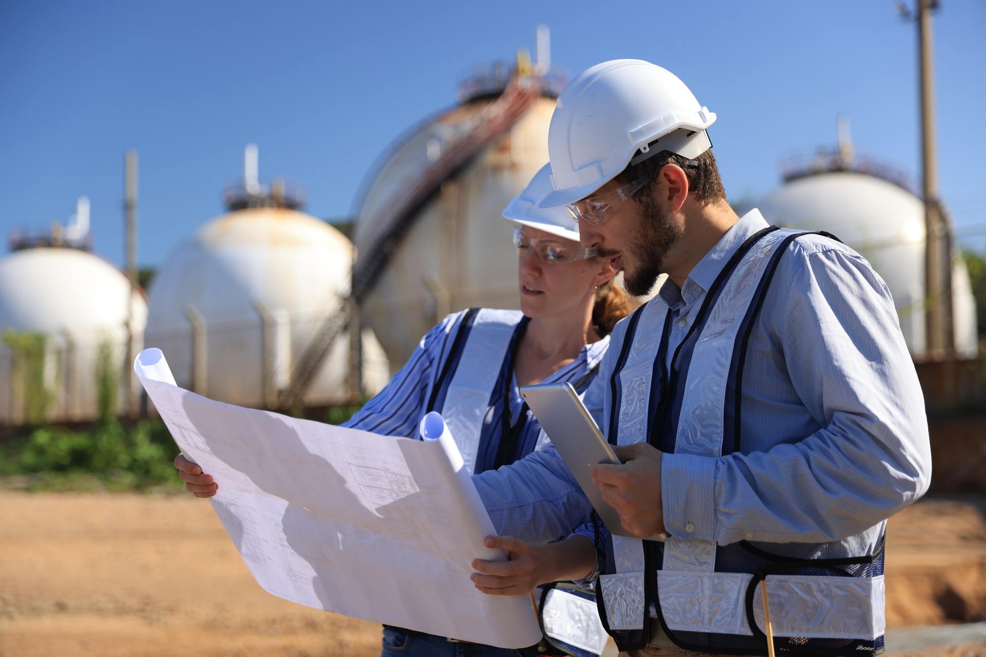 Male & Female engineer stand Discussing building plan at site, Engineers working outdoors against gas containers in the background