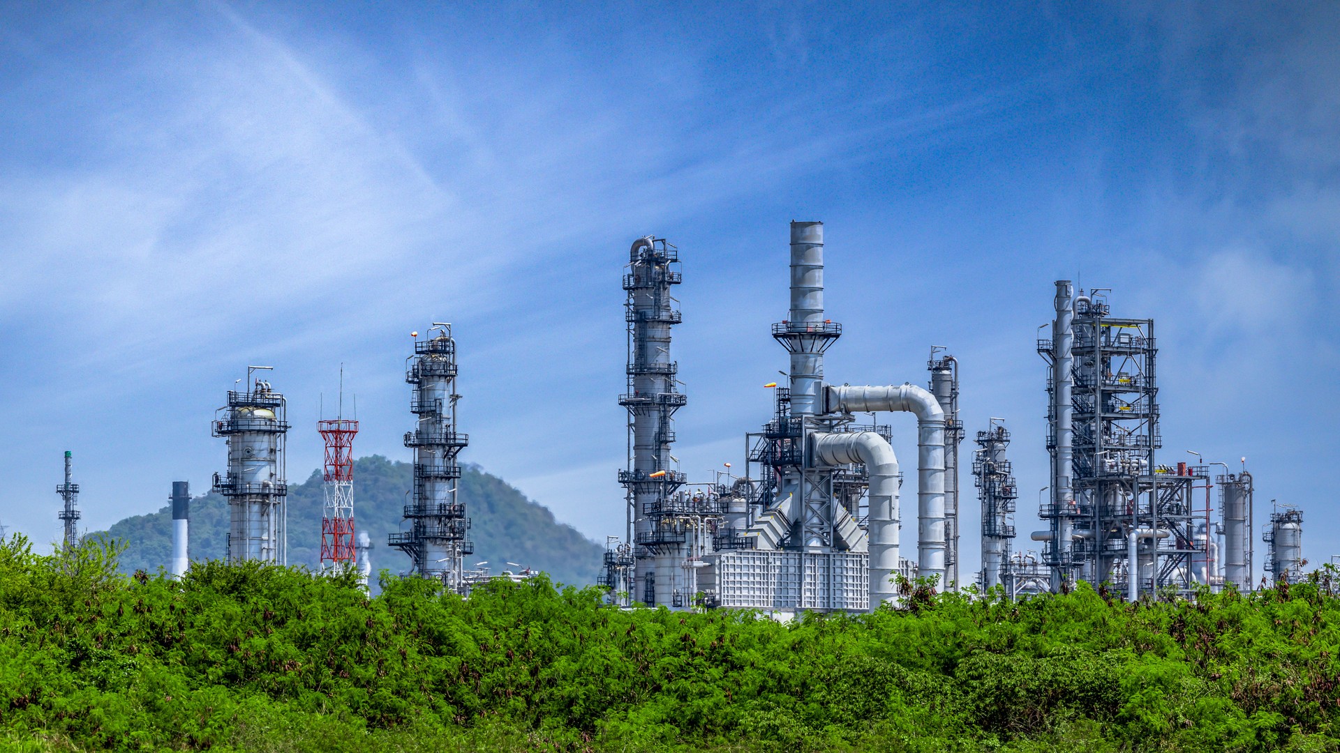 Oil refinery plant from industry zone, Oil and gas petrochemical industrial with tree and blue sky background, Refinery factory oil storage tank and pipeline steel, Ecosystem and healthy environment concepts.